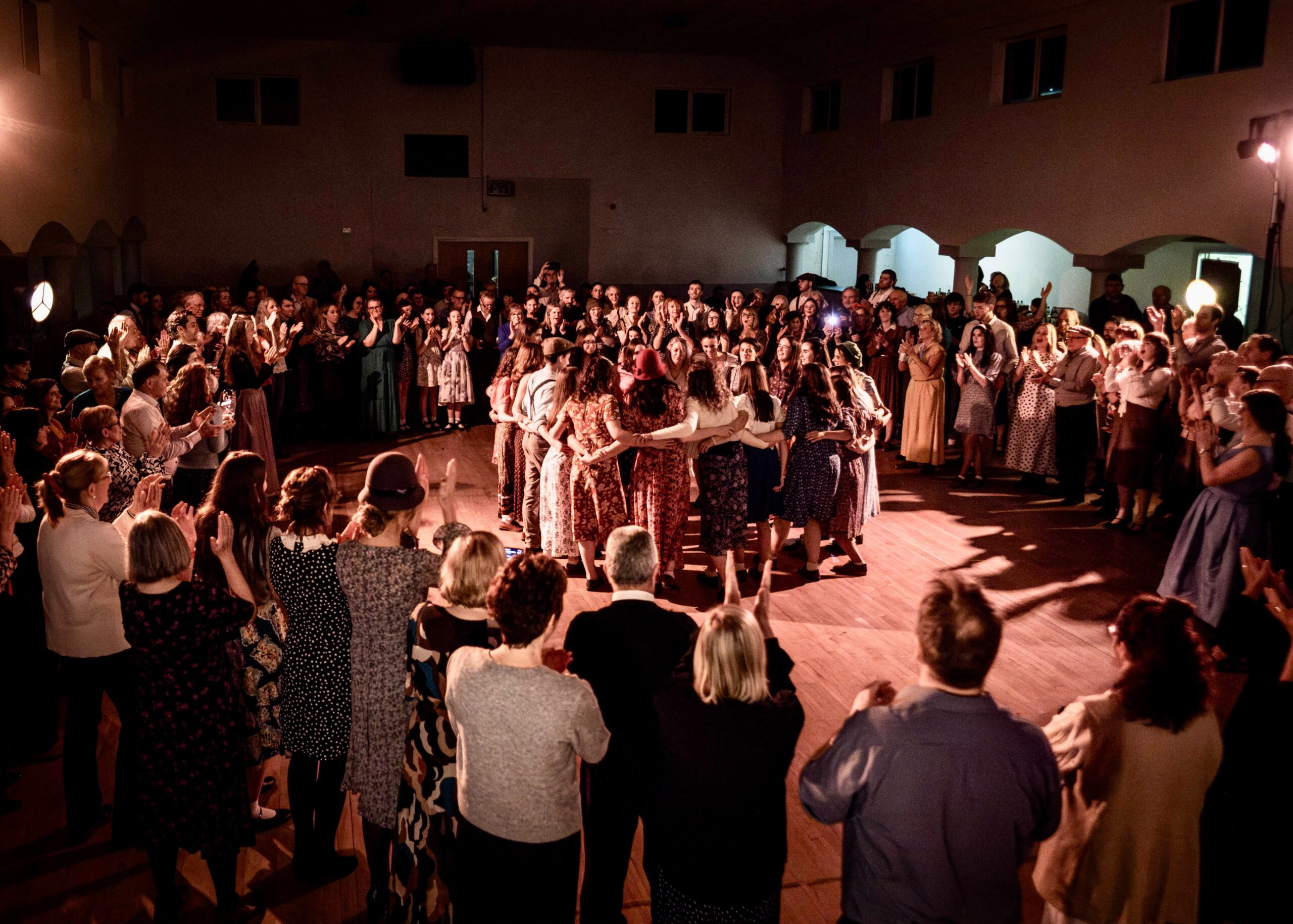 A ring of dancers arm in arm in the middle of the floor, the hall clapping around them.