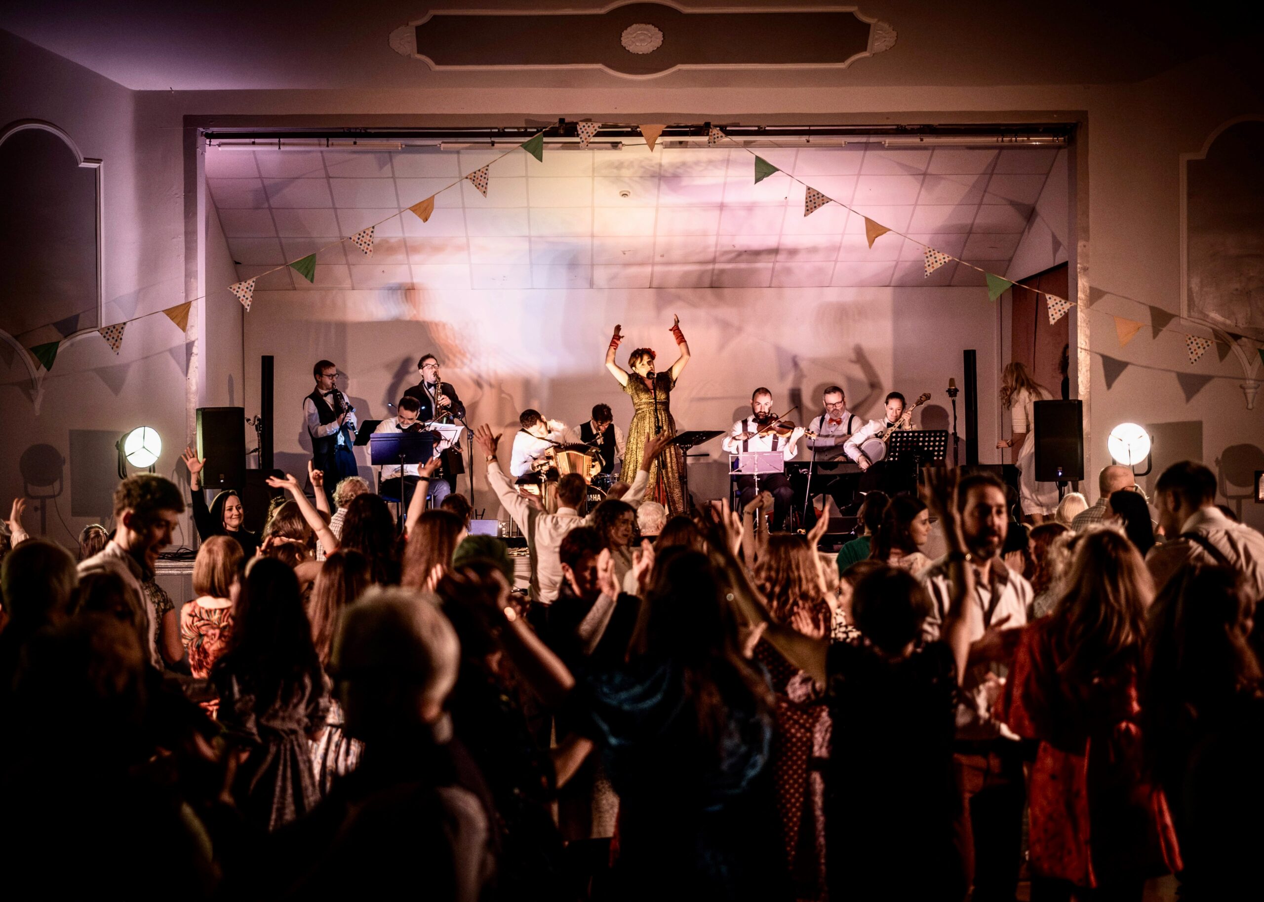 The Gralton Big Band on stage under bunting, a singer in gold with her arms raised and the floor full.